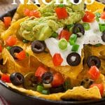 A close up of a plate of nachos with black olives, peppers, sour cream, guacamole ready for game day.
