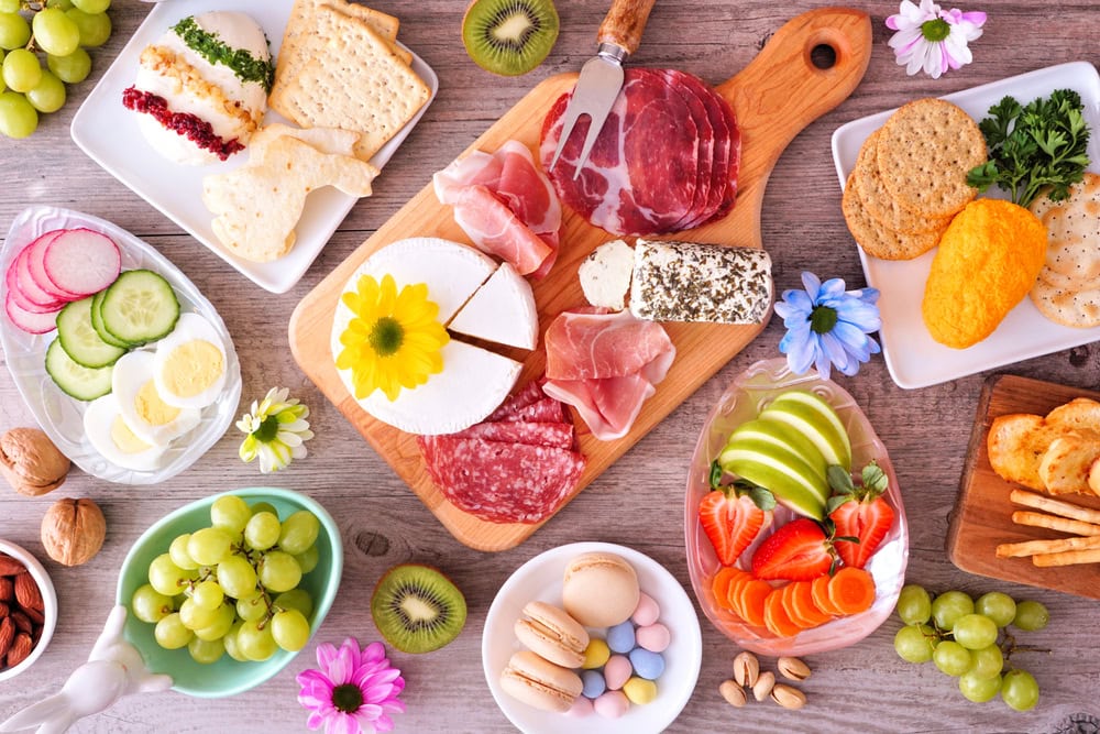 Spring or Easter theme charcuterie table scene against a wood background. Collection of cheese, meat, fruit and vegetable appetizers. Overhead view.