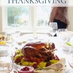 A simple Thanksgiving table with white dishes, stemware and a turkey set on a table in front of a window with a woman looking out the window.