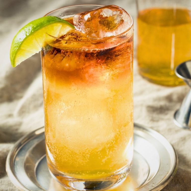 Image of a dark and stormy cocktail on a drink coaster with a slice of lime.