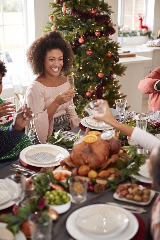Lady sitting at the dining room table with friends toasting each other and smiling with a Christmas tree in the background.